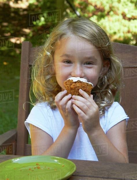 Little Girl Eating a Cupcake at an Outdoor Table - Stock Photo - Dissolve