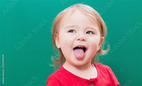 Happy toddler girl sticking her tongue out in front of a chalkboard Stock Photo | Adobe Stock