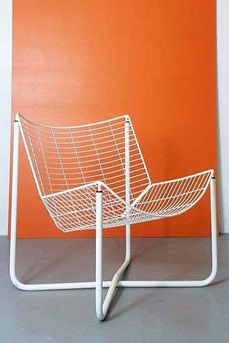 a white wire chair sitting on top of a metal stand in front of an orange wall