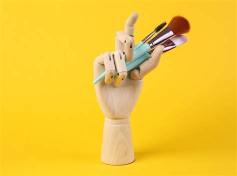 Premium Photo | Wooden hand holds makeup brushes on yellow background