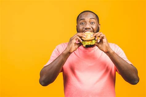 Premium Photo | Young african american man eating hamburger isolated over yellow wall.