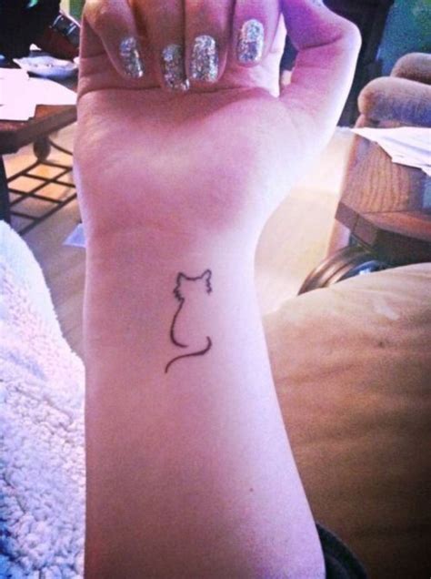 a woman's arm with a small cat tattoo on the left side of her wrist