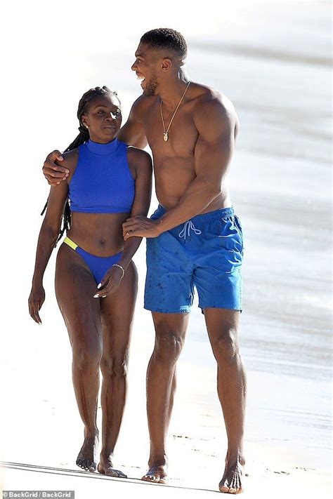 a man and woman walking on the beach in swimsuits, one holding her hand