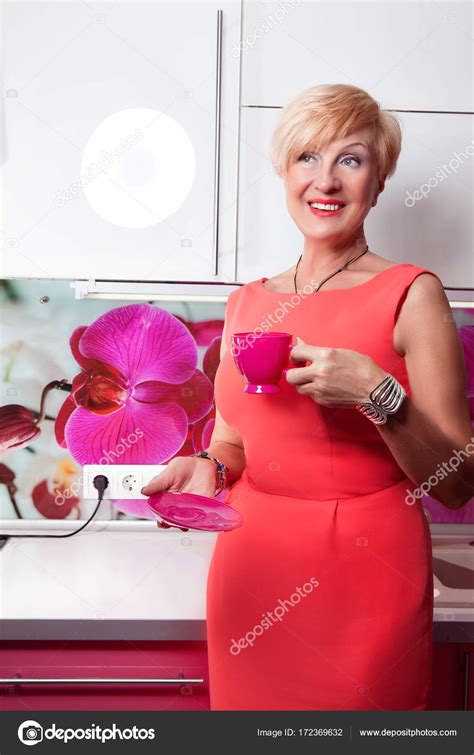 Bright kitchen and happy middle aged woman with red mug of coffee — Stock Photo © Redchanka ...