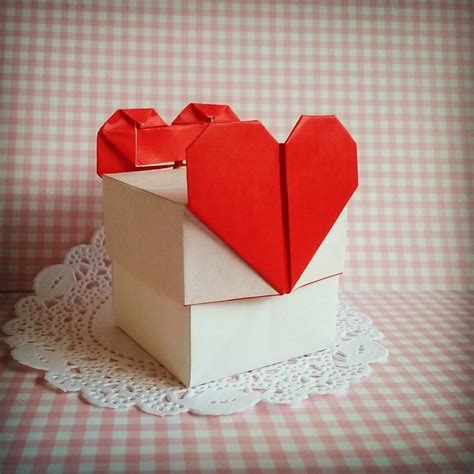 an origami box with two hearts in it sitting on a doily covered table