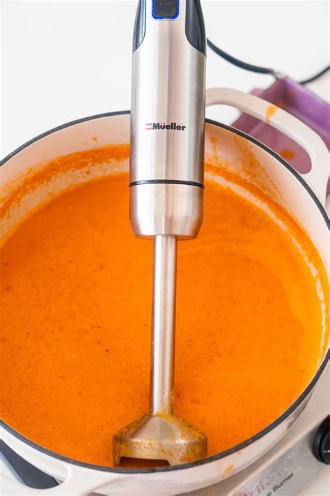 an electric blender is mixing carrots in a pot