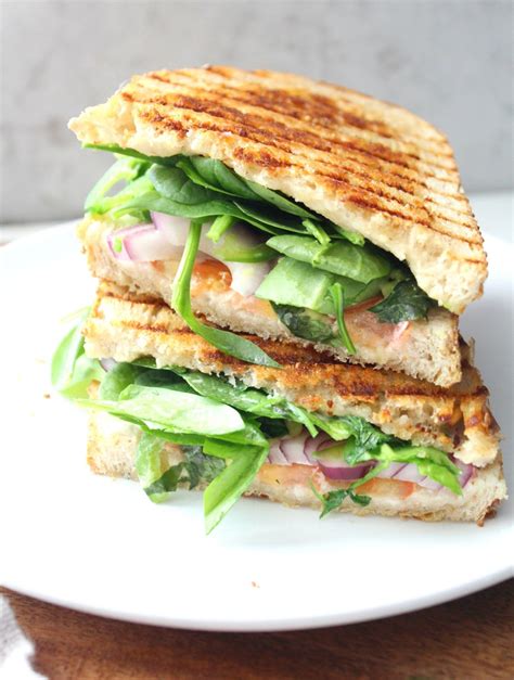 a grilled sandwich with lettuce, tomato and other vegetables on a white plate