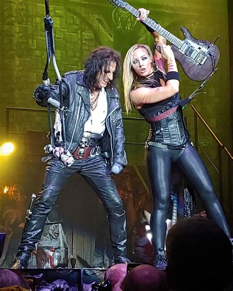 two people on stage with guitars in their hands and one person wearing black leather clothes