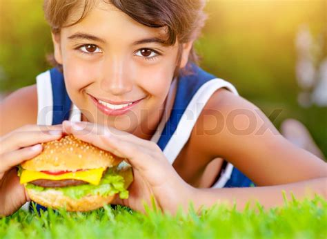 Closeup photo of pretty boy bite tasty big cheeseburger, enjoying picnic outdoors in summer time ...