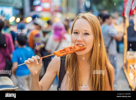 Young woman tourist eating Typical Korean street food on a walking street of Seoul. Spicy fast ...