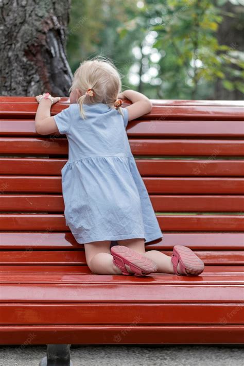Premium Photo | Little girl in blue dress with two ponytails peeks out on bench child in the ...