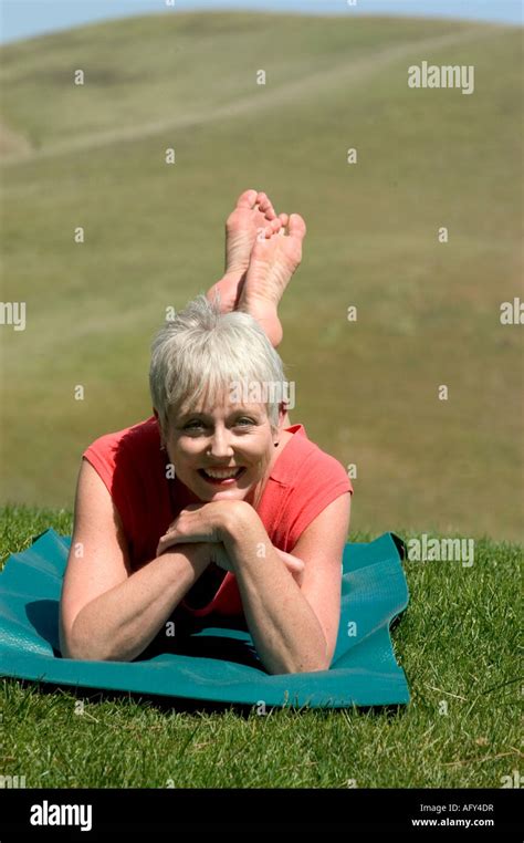 Mature woman baby boomer era practicing yoga positions on a mat, stretching exercising outside ...
