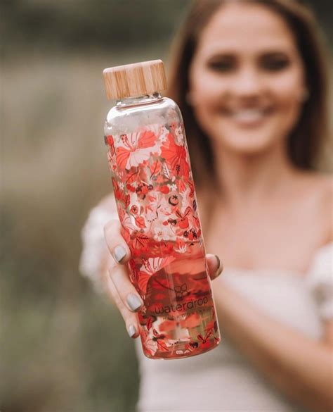 a woman is holding a water bottle with red flowers on it and a wooden lid
