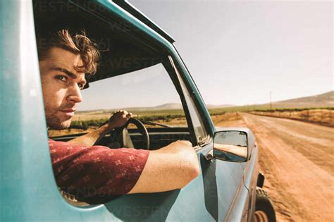 Close up of a man looking out of the window while driving a car. Man driving car on a mud track ...