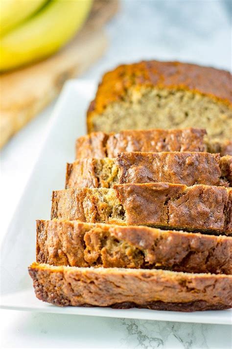 sliced loaf of banana bread on a white plate with bananas in the backround