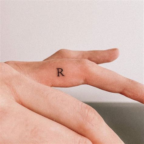 Minimalist letter "R" tattoo on the finger.