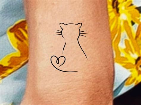 a cat's head with a heart on the left side of its wrist tattoo
