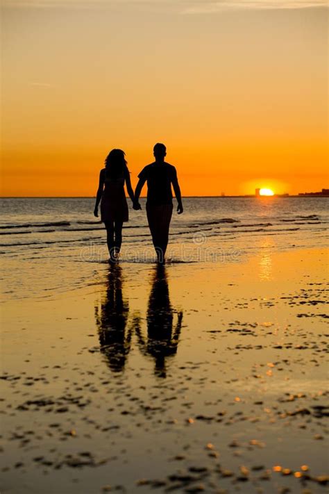 two people walking on the beach holding hands and looking out at the ...