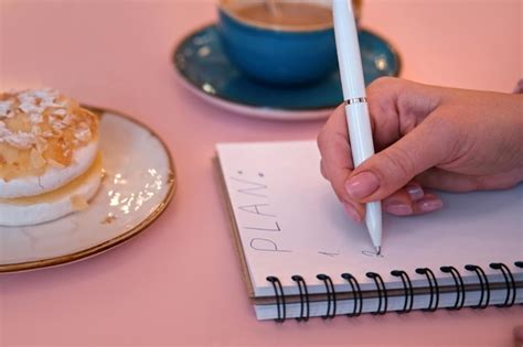 Premium Photo | Woman Writing Plan in a Notepad Sitting on a Pink Cafe Table with Coffee Cup and ...