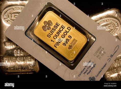 Pure one troy ounce gold bar with assay. Two silver bars in background Stock Photo - Alamy