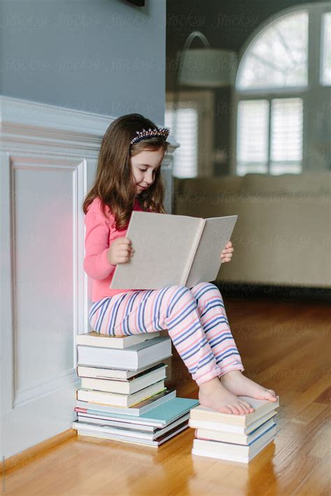 "Cute Young Girl Sitting On A Stack Of Books Reading" by Stocksy ...