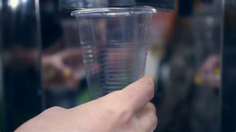 Water flowing into plastic cup. Water cooler. Closeup of hand holding ...