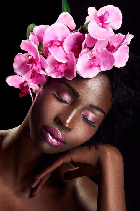 a woman with pink flowers on her head and hands near her face, in front of a black background