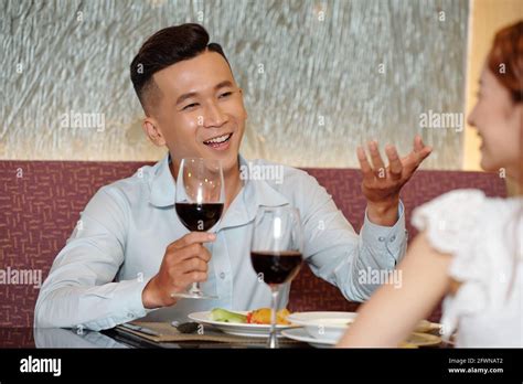 Handsome young man drinking wine and talking with girlfriend at romantic date in restaurant ...