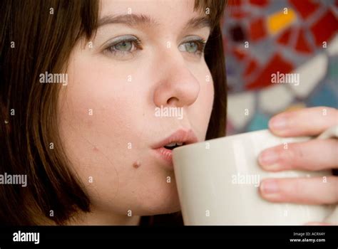 A young woman sips her coffee and talks on the phone as she relaxes in a small coffee shop ...