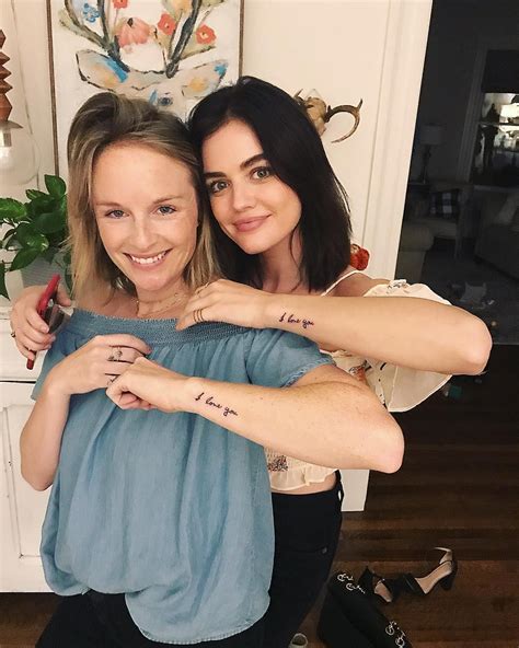 two women hugging each other with tattoos on their arms and chest, both smiling at the camera