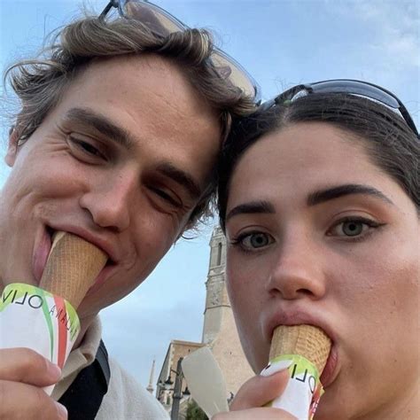 a man and woman are eating ice cream cones in front of a building with a clock tower behind them