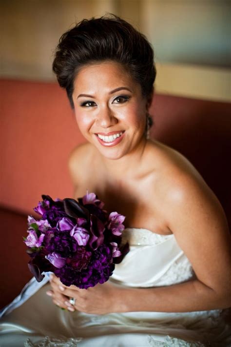 a woman in a wedding dress holding a bouquet of purple flowers and smiling at the camera
