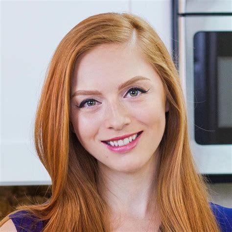 a woman with long red hair and blue eyes smiles in front of a microwave oven