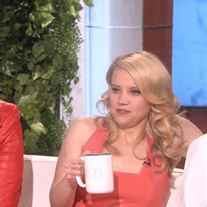 two women sitting at a table with one holding a coffee mug and the other wearing a red dress