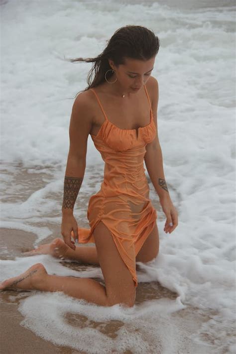 Slim woman in wet tight dress kneeling on seashore · Free Stock Photo