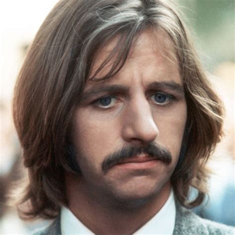 a close up of a person wearing a suit and tie with a moustache