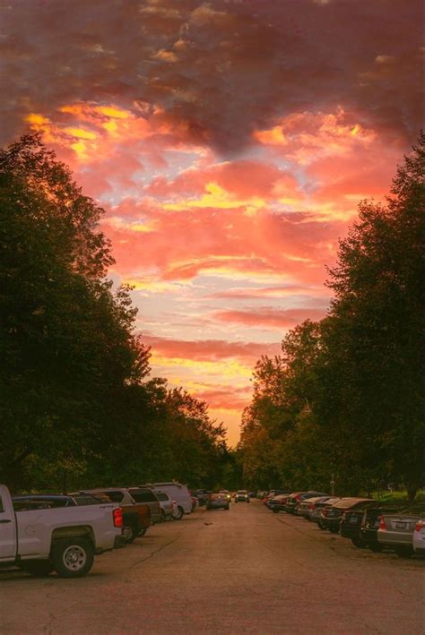 a parking lot filled with lots of parked cars under a colorful sky at ...