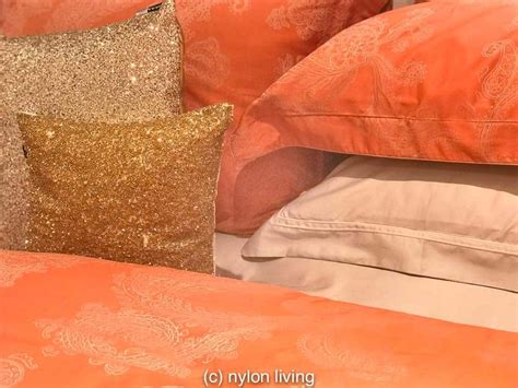 an orange and gold bed with two pillows on top of each other, next to a ...