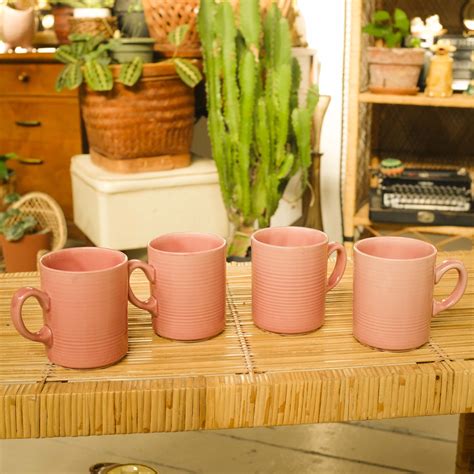 four pink mugs sitting on top of a table next to a potted plant
