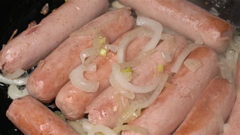 Sausages with onion fried in black pan with oil. Close-up view of cooking of delicious, high ...