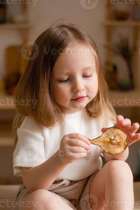 cute little girl eats natural pastille at home in a wooden kitchen. Food for children from ...