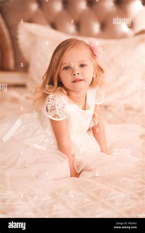 Cute baby girl 3-4 year old wearing stylish white dress sitting in bed ...