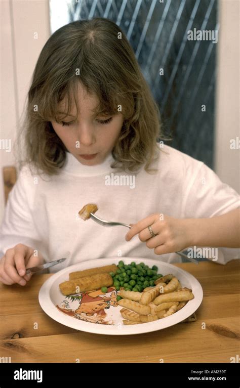 seven year old girl eating fish fingers chips and peas at the table Stock Photo - Alamy