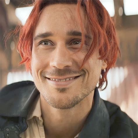 a smiling man with red hair and piercings on his ears is looking at the camera