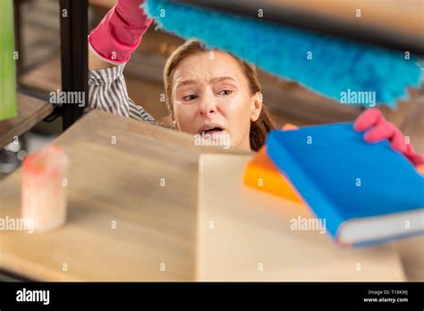 Mature housewife dusting the bookcase feeling sensitive to dust Stock Photo - Alamy