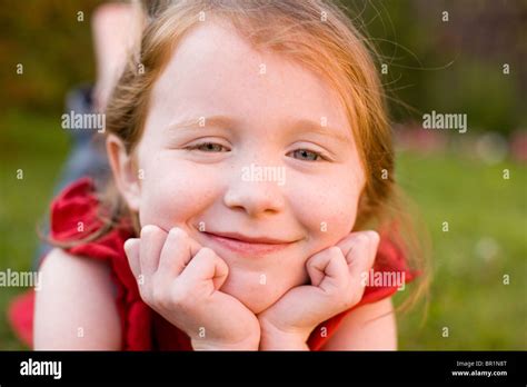 Small Blue-Eyed Girl in Red T-Shirt Lying on Green Grass Smiling as She Relaxes her Chin in Her ...