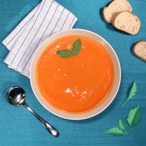 a bowl of carrot soup next to some slices of bread on a blue tablecloth