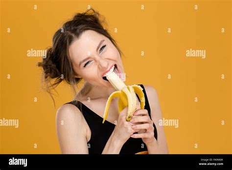 Portrait of funny beautiful young woman eating banana over yellow background Stock Photo - Alamy