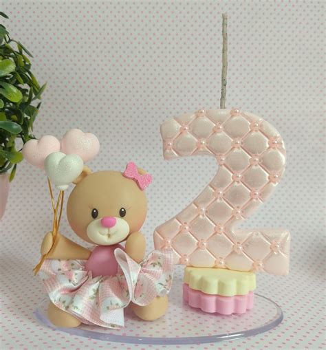 a small teddy bear holding balloons in front of a number two cake on a plate