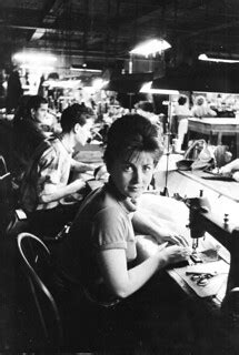 Men and women sew on machines in a large garment shop. | Flickr